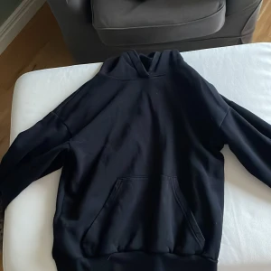 Svart hoodie från H&M med ficka - Svart hoodie från H&M i storlek 158/164. Tröjan har en klassisk huva och en stor magficka framtill. Materialet är mjukt och känns skönt mot huden, perfekt för chill dagar. Långärmad och med ribbade muddar vid ärmslut och nederkant.