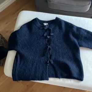 Mörkblå stickad kofta från Gina Tricot - Säljer en mörkblå stickad kofta från Gina Tricot i storlek 158/164. Koftan har snygga knytband framtill och en mjuk, fluffig struktur. Perfekt för dig som gillar en chill och mysig stil med lite extra detaljer.