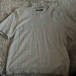 Beige stickad tröja från Gina Tricot - En enkel och stilren beige stickad tröja från Gina Tricot i storlek XS. Tröjan har korta ärmar, rund halsringning och ribbade kanter vid ärmslut och nederkant. Perfekt för lager-på-lager och passar till allt.