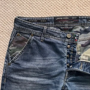Jacob cohën jeans type 613 c  - Jacob cohën jeans campflage pattern inuti och Loggan. Väldigt trevliga i storleken W34 men passar mer W32/33. Mått A: 43 cm B: 98 cm. Inga större defekter men dom är använda och lite slitna på vissa ställen vilket jag personligen tycker dom blir snyggare av! ☺️