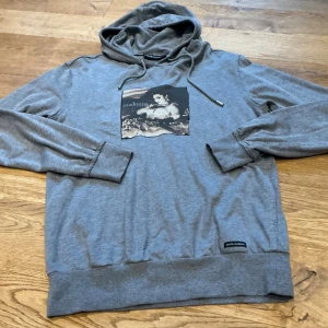 Dolce & Gabbana- Tröja, Hoddie med tryck  ”Madonna - Like a Virgin” - Dolce & Gabbana- Tröja, Hoddie med tryck  "Madonna - Like a Virgin" Ett sällsynt samlarobjekt för Madonna- och modeälskaren! Säljer en autentisk, grå huvtröja från Dolce & Gabbana med ett stort tryck av Madonna från hennes ikoniska "Like a Virgin" era. Trycket inkluderar texten "madonna like a virgin" och årtalet © 2012 Boy Toy, Inc. -Material: 100% bomull, mjuk och dyr bomull, Grå (melerad) -Storlek på etiketten *Observera: Den italienska storleken 44 är relativt liten, kontrollera måtten noga 