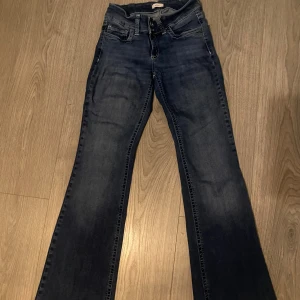 Mörkblå bootcut jeans med broderi - Snygga mörkblå jeans med bootcut passform och klassisk femficksdesign. Baktill finns coola broderade detaljer på fickorna. Jeansen är lågmidjat och är tillverkade i slitstarkt denimtyg. Perfekta för dig som gillar retrovibbar och vill sticka ut lite extra.
