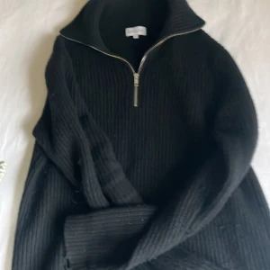 Svart stickad half zip-tröja Davida cashmere - Svart stickad tröja från Davida i storlek S med ribbad struktur och half zip-dragkedja framtill. Tröjan har hög krage och långa ärmar, perfekt för dig som gillar en clean och stilren look. Snygg att bära till jeans eller chinos. Modellen på bilden är 180 cm. Nypris 3000kr