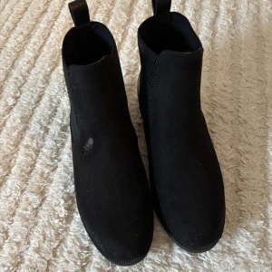 Svarta chelsea boots från Anna Field - Snygga svarta chelsea boots från Anna Field med elastiska paneler på sidorna och dragflik baktill. Bootsens ovandel är i mocka-look och har en rund tå samt platt sula. Perfekta för dig som gillar stilrena och klassiska skor med modern vibe. Det finns en liten fläck på höger sko som man kan tvätta bort,Använda 2gånger.
