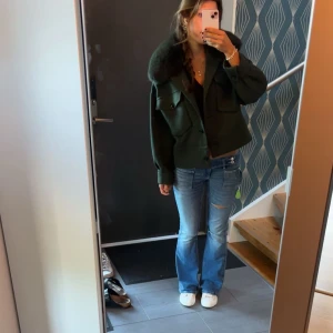 Mörkgrön kappa med päls från Meotine - Säljer en mörkgrön kappa från Meotine med stor fluffig päls på kragen. Jackan har en loose passform, stora fickor med knappar och är riktigt snygg till jeans. Perfekt för dig som vill ha en cool och varm jacka med statementkrage.