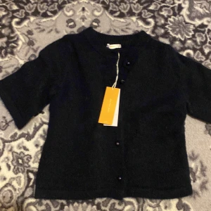 Svart kofta från Gina Tricot - Svart kofta från Gina Tricot med kort ärm och rund hals. Koftan är stickad och har snygga svarta knappar framtill. Perfekt att slänga över en topp för en chill look.