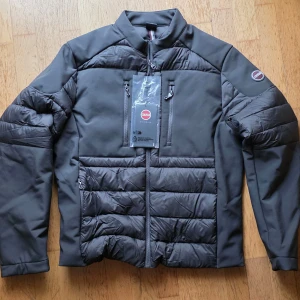 Mörkgrå dunjacka från Colmar Storlek 52 Ny oanvänd  - Snygg mörkgrå/antracit dunrjacka från Colmar Jackan har en dragkedja framtill, två fickor med dragkedja på framsidan och en liten Colmar-logga på vänster ärm. Den har även en vadderad design på fram- och baksidan samt ärmarna.  Ny med taggar Storlek 52