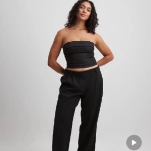 Svart bandeau tubtopp med dragkedja - Säljer en svart bandeau tubtopp med stilren design och dragkedja i ryggen. Toppen är axelbandslös och har en croppad passform som sitter tight. Perfekt att styla med höga byxor eller kjol för en trendig look.