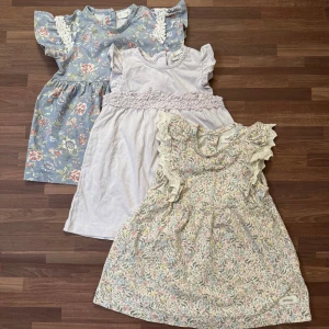 Set med 3 klänningar, 74 - Tre urgulliga klänningar från Newbie i storlek 74 (6-9mån). Alla med volangärmar, fina spetsdetaljer och knäppning bak. Använd fåtal gånger och i mycket god skick. Har en till av den blommiga klänningen längst ner, säljes separat på min profil, samma storlek.