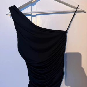 Svart one shoulder topp BikBok XS - Snygg svart topp från BikBok i storlek XS. Toppen är one shoulder med en smal axelrem och draperad effekt längs hela plagget. Pris kan diskuteras!