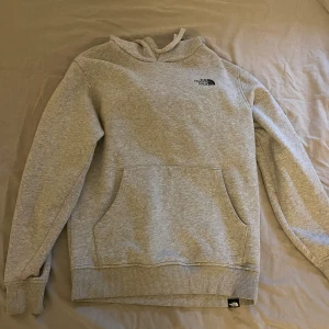 Grå hoodie från The North Face M - Säljer en grå hoodie från The North Face i storlek M. Tröjan har huva med snörning, stor magficka och tryck med logga på bröstet samt ett stort gult och svart tryck på ryggen. Tillverkad i mjuk bomullsmix, perfekt för chill dagar.