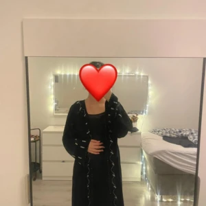Svart långklänning med volangdetaljer Man kan säga som en abaya  - Säljer en svart långklänning med snygga volangdetaljer längs kanterna. Klänningen har långa ärmar och en rak, elegant siluett. Perfekt för dig som gillar en stilren look med en twist.