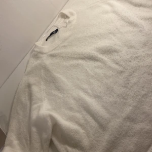 Vit stickad tröja från 157 - Mysig vit stickad tröja från 157 i storlek M. Tröjan har rund hals och långa ärmar med ribbade muddar. Perfekt för dig som gillar enkel och clean stil med mjukt material som känns skönt mot huden.