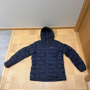 Mörkblå dunjacka med huva - Peak Performance dunjacka i mörkblå färg. Jackan är köpt i peak butiken och har använts en del. Fortfarande hel och ganska fin men har tecken på användning. Storleken är M