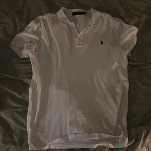 Vit Polo Ralph Lauren t-shirt M - Vit t-shirt från Polo Ralph Lauren i klassisk pikéstil med korta ärmar och krage. Ikonisk broderad logga på bröstet. Tillverkad i mjuk bomull som känns skön mot huden. Perfekt för dig som gillar stilrena och tidlösa plagg.