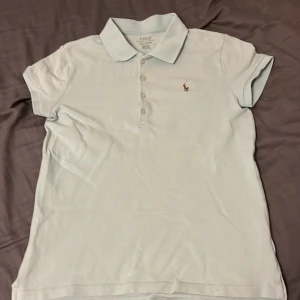 Mint grön pikétröja från Polo Ralph Lauren - Snygg mint grön pikétröja från Polo Ralph Lauren med klassisk krage och korta ärmar. Tröjan har knappar framtill och den ikoniska broderade loggan på bröstet. Tillverkad i mjuk bomull som är skön mot huden. Perfekt för en chill och stilren look.