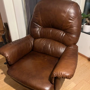 Fåtölj + pall - Säljer en mycket bekväm och stilren fåtölj i mörkbrunt äkta läder med tillhörande fotpall. Fåtöljen har ett klassiskt snurrstativ i trä och mjuk stoppning som ger utmärkt sittkomfort. Perfekt för vardagsrummet, läshörnan eller kontoret.