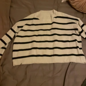 Vit och svart randig stickad tröja - Säljer en vit stickad tröja med svarta horisontella ränder. Tröjan har lång ärm, ribbad kant vid hals och nederdel samt en lite högre halsringning. Perfekt för dig som gillar klassisk och chill stil.