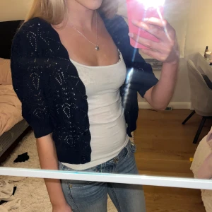 Mörkblå stickad kofta från Kappahl - Supersöt mörkblå stickad kofta från Kappahl med kortare passform och v-ringad hals. Koftan har ett snyggt hålmönster, tre knappar framtill och ribbade muddar vid ärmarna. Perfekt att slänga över ett linne eller t-shirt för en chill look.