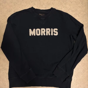 Svart sweatshirt från Morris Gents - Svart sweatshirt från Morris Gents i storlek M med vit broderad logga framtill. Tröjan har rund hals, ribbade muddar vid ärmslut och nederkant samt långärmad passform. Perfekt för dig som gillar stilrena och klassiska plagg med tydlig branding.