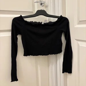 Svart croppad topp från H&M Divided - Svart ribbad croppad topp från H&M Divided med lång ärm och offshoulder-design. Toppen har vågiga kanter. Använd endast en gång! Vid intresse skickar jag gärna fler bilder😁💕
