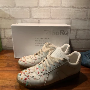 Masion margiela gats  - Maison Margiela  sneakers i vitt skinn med coola färgstänk i rött, blått, orange och svart på tån och sidorna. Klassisk låg modell med snörning och gummisula. Tillverkade i lamm- och kalvskinn, med en unik konstnärlig vibe som sticker ut.