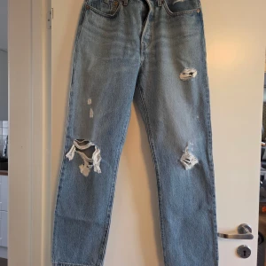 Levi's 501 ljusblå ripped jeans, W27 L28 - Säljer ett par Levi's 501 Premium jeans i ljusblå tvätt med snygga slitningar och hål på benen för en cool, avslappnad vibe. Klassisk rak passform, fem fickor och knappgylf. Perfekta för dig som gillar vintage och streetstyle. Knappt använda. 