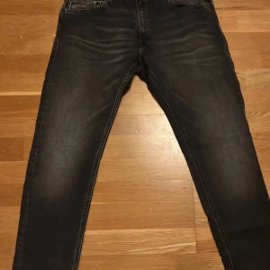 Replay svart/grå jeans - Svarta jeans från Replay med snygg tvätt och klassiska fem fickor. Modellen är skinny med smal passform och raka ben. Jeansen har dragkedja och knapp framtill samt detaljerade bakfickor. Perfekta för dig som gillar stilrena och moderna jeans.