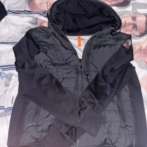Svart pufferjacka Parajumpers  - Svart pufferjacka från Parajumpers med huva och quiltad framsida. Jackan har dragkedja, ribbade muddar och två sidofickor med dragkedja. Ärmar och rygg är i mjuk fleece, medan framsidan är glansig och quiltad. Märkespatch på ena ärmen. Den är knappt använd max 10 ggr inga spår på att den är använd precis som helt ny. Priset kan alltid diskuteras så våga ge ett pris. Ifall du funderar över något hör alltid av dig. Jackan är i XXL men Passar XL oxå men kan även passa långa som väger 73 uppåt.