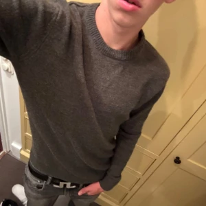 Mörkgrön stickad tröja herr - En stilren mörkgrön stickad tröja med rund halsringning och långa ärmar. Tröjan har en klassisk passform och är perfekt för lager-på-lager under kyliga dagar. Enkel att matcha med både jeans och chinos. Från solid.