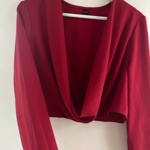 Röd croppad blus med djup v-ringning - Röd croppad blus med lång ärm och djup v-ringning. Toppen har en snygg draperad front. Sista bilden är samma blus dock i en annan färg. Älskar dessa men passar inte i röd - den är helt oanvänd.                                                                                           (Läs alltid min profil för villkor)