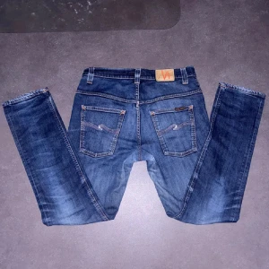 Blåa Nudie jeans organic denim - Snygga blå jeans från Nudie Jeans med klassisk femficksdesign och kontrastsömmar. Jeansen har mellanblå tvätt och detaljerade bakfickor med Nudie-loggan. Pris går att diskutera.