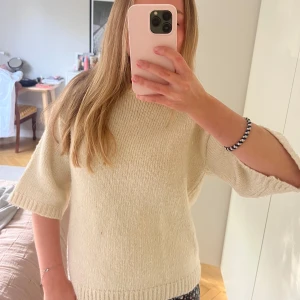 Beige stickad tröja med halvärm - Mysig beige stickad tröja med rund halsringning och halvärmar. Tröjan har en rak passform och ribbade muddar vid ärmslut och nederkant. Perfekt för lager-på-lager under höst och vinter.