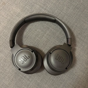 JBL Over-Ear Wireless Headphones - Snygga svarta JBL over-ear hörlurar med trådlös anslutning. Mjuka öronkuddar och justerbar bygel för bekväm användning. Hörlurarna är i gott skick utan synligt slitage eller defekter. Perfekt för musik, film och samtal med hög ljudkvalitet.