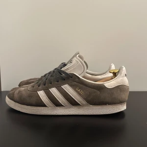 Gråa Adidas Gazelle sneakers  - Säljer ett par gråa  klassiska Adidas Gazelle sneakers. Storlek 43 1/3. Bra skick finns defekter som ett litet hål i sulan men annars fina.