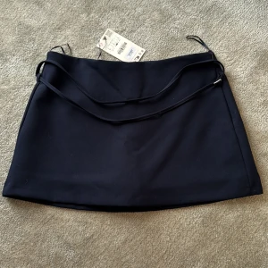 Mörkblå kortkjol med snörning från Zara - Aldrig använda, Stilrena mörkblå mini kortkjol från Zara med smal snörning i midjan och inbyggda shorts under. Små i storleken jag har vanligt vis L-M i kjolar denhär va för liten så skulle säga att den sitter perfekt på en s/m.💕💕💕