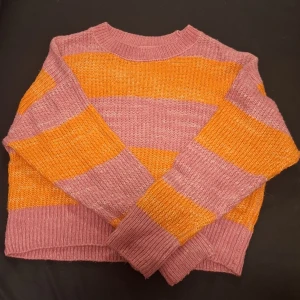 Randig stickad tröja från Kappahl - Superfin stickad tröja från Kappahl i storlek S. Tröjan har breda ränder i rosa och orange, rund halsringning och långa ärmar. Perfekt för dig som gillar färg och vill ha en mysig och trendig look.