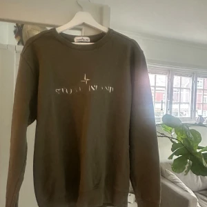 Grön sweatshirt från Stone Island - Säljer en grön sweatshirt från Stone Island med logga och kompassdetalj framtill. Tröjan har rund halsringning och långa ärmar, perfekt för en chill och stilren look. Materialet är mjukt och skönt, passar till många outfits.skriv för mer frågor !🤗