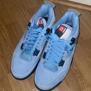 Nike Air Jordan 4 University Blue - Säljer ett par Nike Air Jordan 4 University Blue sneakers med ljusblå mocka, svarta och grå detaljer samt klassisk Jumpman-logga på hälen.  Perfekta för dig som vill sticka ut med en ikonisk och stilren sneaker. Helt ny i skick, använt 2-3 gånger, box medföljer. ÄKTA SÅKLART!
