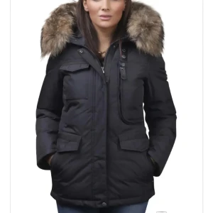 Svart hollies jacka med pälsluva - Säljer en svart holliesjacka med stor, fluffig päls runt luvan. Jackan har flera fickor framtill, dragkedja och knappar samt en klassisk, rak passform. Perfekt för kalla dagar och riktigt snygg till jeans.