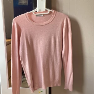 Ljusrosa stickad tröja från Moda Impresion - Superfin ljusrosa stickad tröja från Moda Impresion. Tröjan har rund halsringning, långa ärmar och ribbade muddar vid ärmslut och nederkant. Perfekt för dig som gillar en enkel och stilren look med mjukt material.