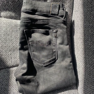 Svarta Replay jeans LUZ 27/30 - Snygga svarta jeans från Replay i modellen LUZ. Klassisk femficksdesign med diskreta sömmar och Replay-lapp bak i midjan. Jeansen är i stretchigt material som sitter skönt och har en smal passform. Perfekta till en cool streetstil.