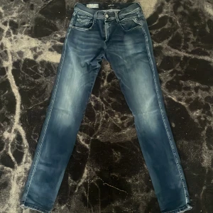 Replay Anbass Hyperflex jeans blå - Slim fit jeans från Replay, modell Anbass Hyperflex. Snyggt tvättade i blå nyans med ljusa slitningar och klassisk femficksdesign. Storleken är W29 