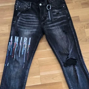 Svarta Amiri jeans med färgstänk - Snygga svarta jeans från Amiri med coolt färgstänksmönster och stor logga på ena benet. Jeansen har slitna detaljer och en slim passform. Klassisk femficksmodell med dragkedja och knapp. Perfekta för dig som vill sticka ut med din stil. Passar perfekt nån som är 180 cm  170 cm går det också men då går det o vicka så 