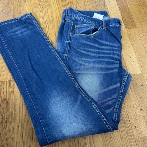 Blå slim jeans från 1953 Denim Brand - Snygga blå jeans från 1953 Denim Brand i slim fit-modell. Jeansen har klassisk femficksdesign, ljusa slitningar och kontrastsömmar. Perfekta för dig som gillar en smalare passform och vill ha en tidlös look.