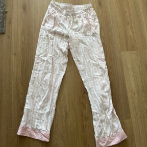Rosa och vita randiga pyjamasbyxor från Victoria Secret  - Supermysiga pyjamasbyxor i rosa och vitt med randigt mönster från Victoria Secret. Byxorna har resår och snörning i midjan, två fickor fram och ljusrosa muddar med prickar längst ner. Tillverkade i bomull och polyester, perfekta för chill dagar hemma. Byxorna är slitna längst ner i ena benet. 