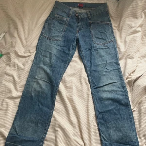 Unika Levis jeans - Säljer ett par blå jeans från Levis med raka ben och unika fickor både fram och bak. Jeansen har klassisk denimlook, kontrastsömmar och knappstängning.