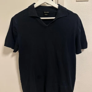 Svart t-shirt med krage från Massimo Dutti - Stilren svart t-shirt från Massimo Dutti med klassisk krage och v-ringning. Tillverkad i en skön mix av bomull och linne, perfekt för en clean och avslappnad look. Kortärmad modell som passar till det mesta.