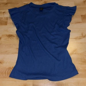 Blå ribbad topp med volangärm Shein XS - Säljer en blå ribbad topp från Shein i storlek XS. Toppen har korta volangärmar och rund halsringning. Materialet är stretchigt och bekvämt, perfekt för en chill och snygg look. Enkel att matcha med både jeans och kjol.