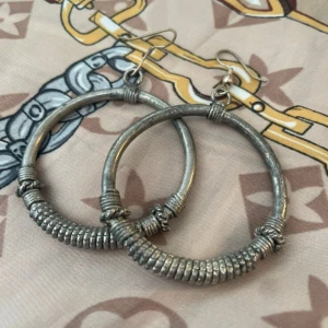 Stora silverfärgade hoops örhängen - Säljer ett par chunky hoops örhängen i silverfärgad metall. De är runda och har coola detaljer med lindade metalltrådar runt ringen som ger en rå och edgy vibe. Perfekt för dig som gillar statement-smycken och vill sticka ut.